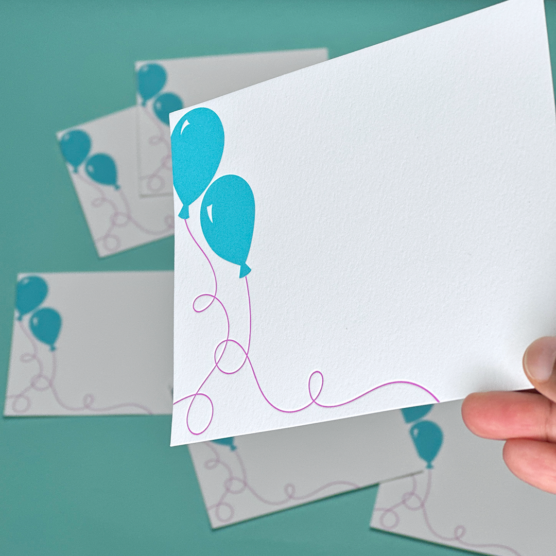 A hand holding a notecard with balloons