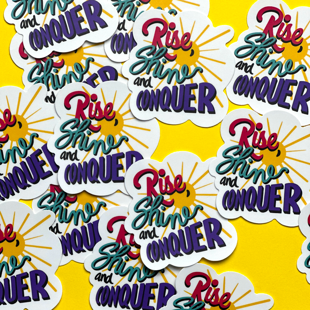 A flat lay of multiple stickers with the words rise, shine and conquer.