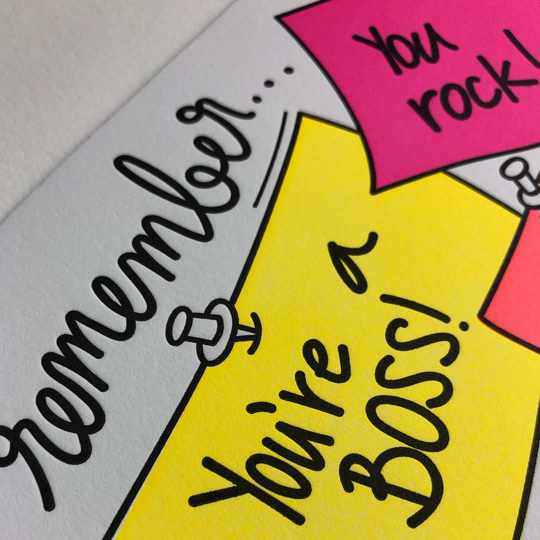 A close up shot of a greeting card showing the paper texture and a sticky note image with the words You're a boss and You rock.