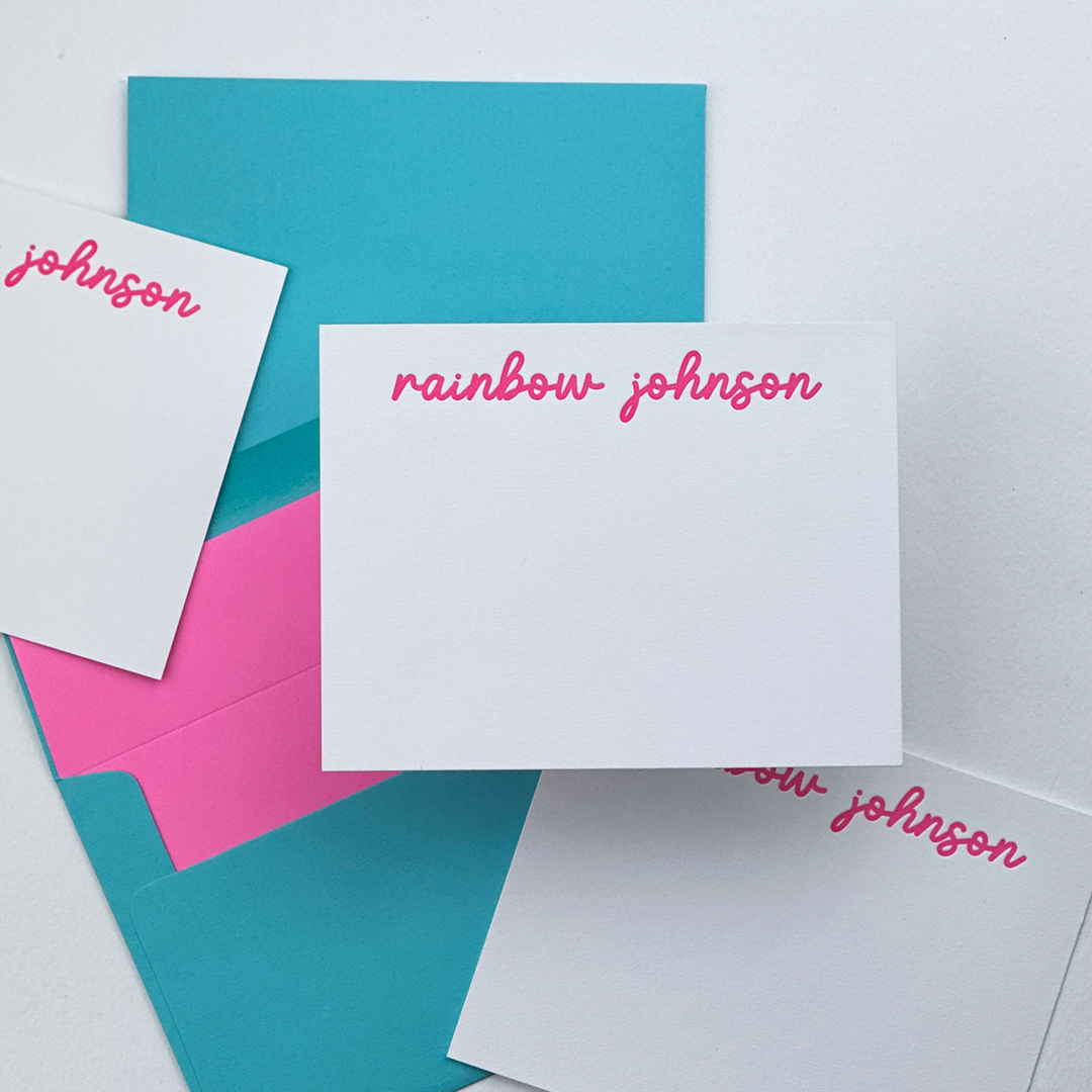 Letterpress Printed Note cCrds in a Flatlay with lined envelopes.  The Cards have the name Rainbow Johnson printed in pink ink. 