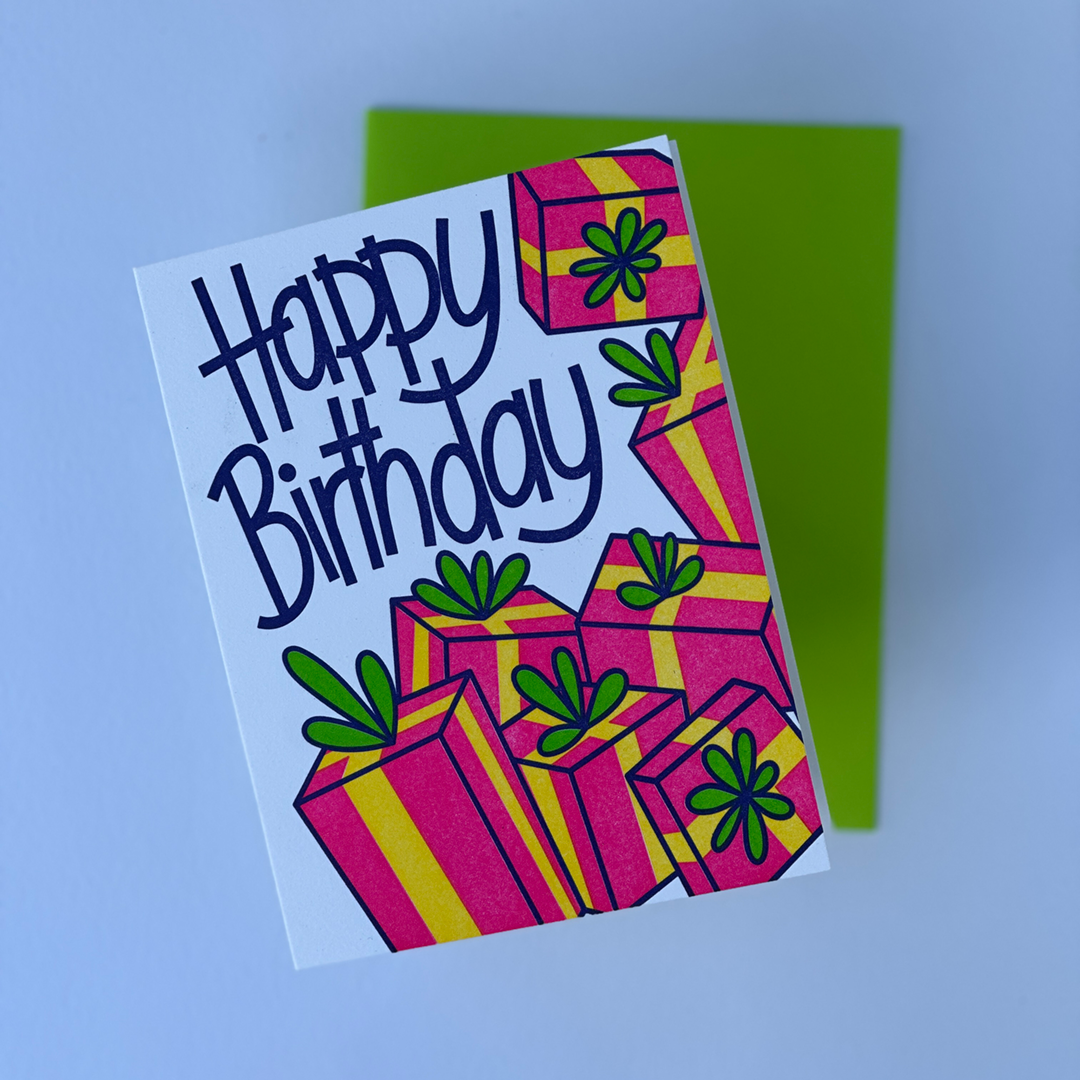 A Greeting Card with the words Happy Birthday and a design with a lot of gifts. The card is in a flat lay with a matching envelope. 