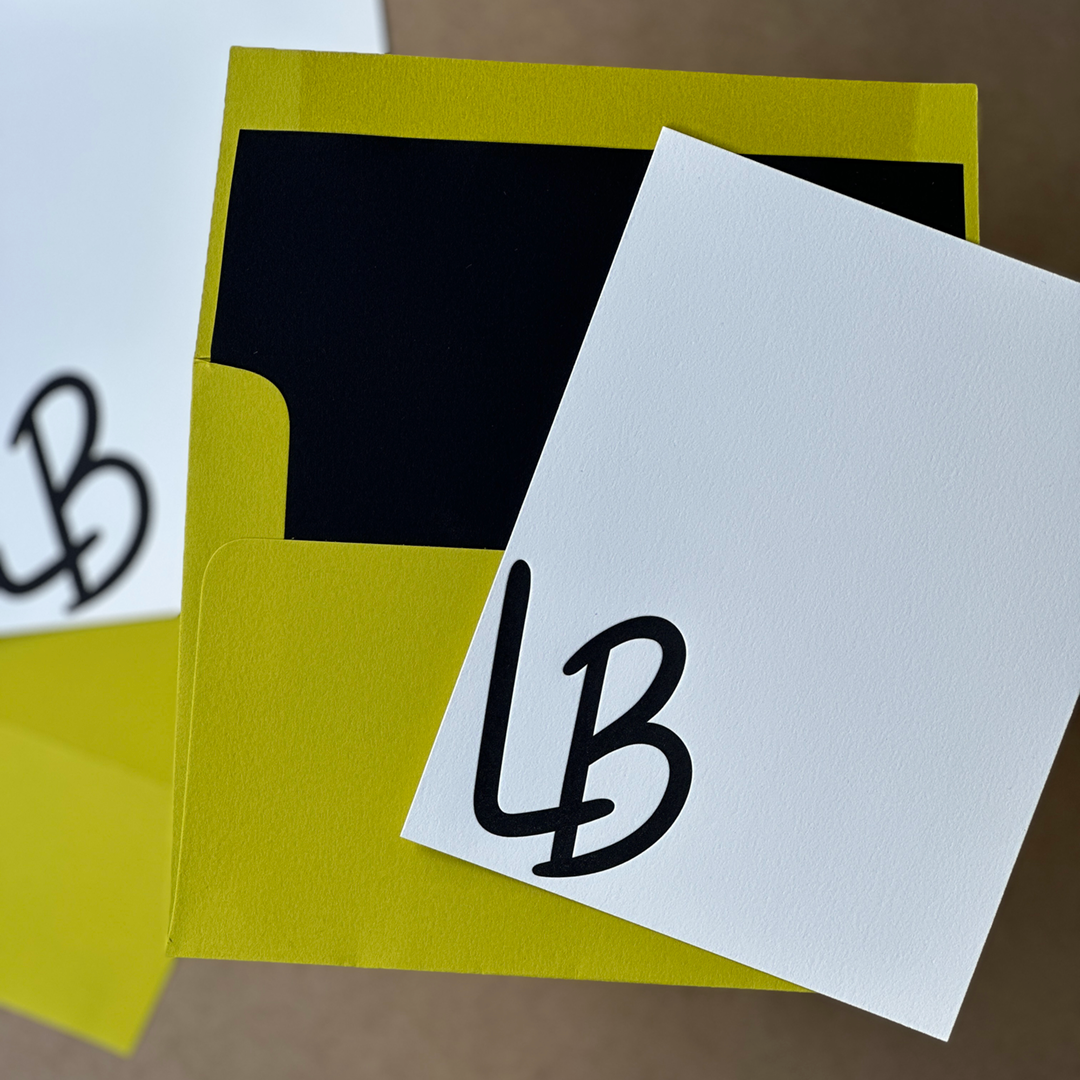 An lined envelope laying flat with a notecard Letterpress printed with the initials L and B. 