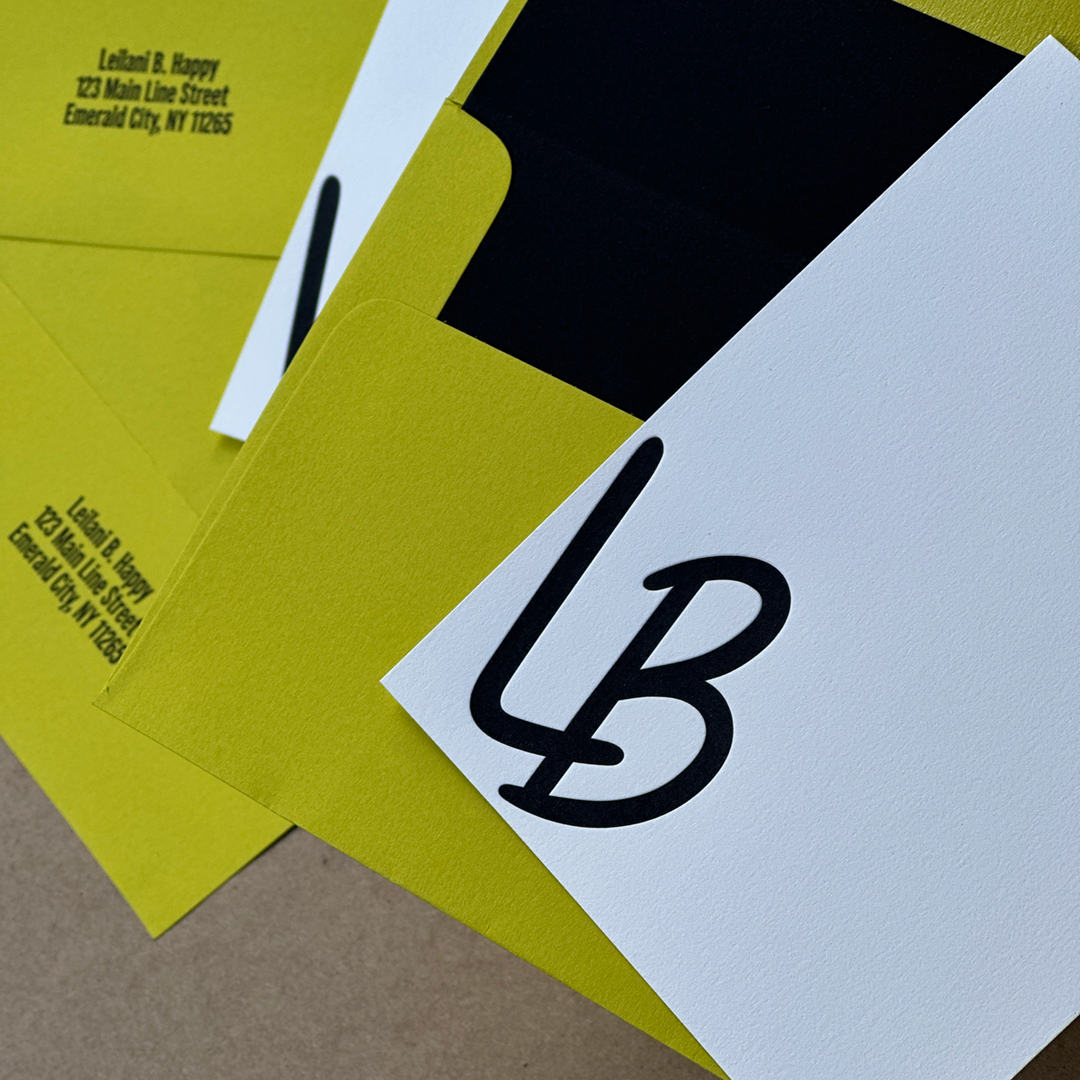 Multiple envelopes in a flat lay with a Letterpress printed notecard on top.  The notecard has the  initials L and B. 