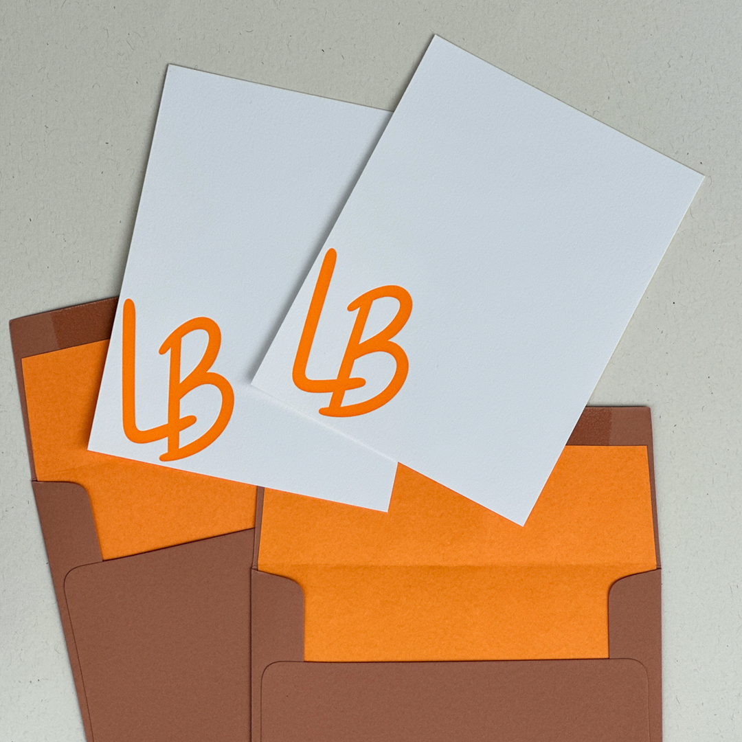 Two Letterpress Note Cards with the initials LB printed in Orange ink in a flat lay with two lined envelopes. 