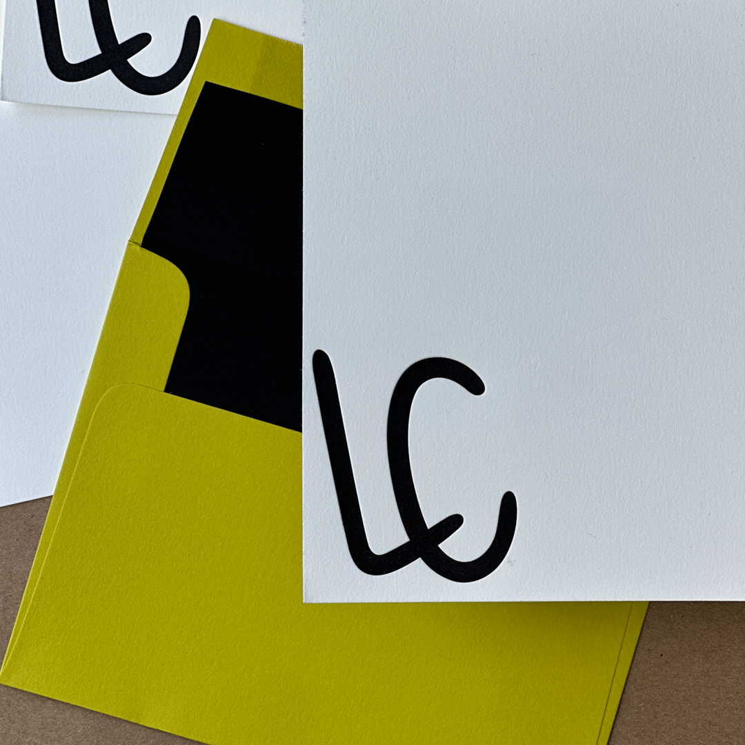 A close-up of the corner of Letterpress Stationery with the initials "LC" printed in Black and a Chartreuse envelope lined in Black. 